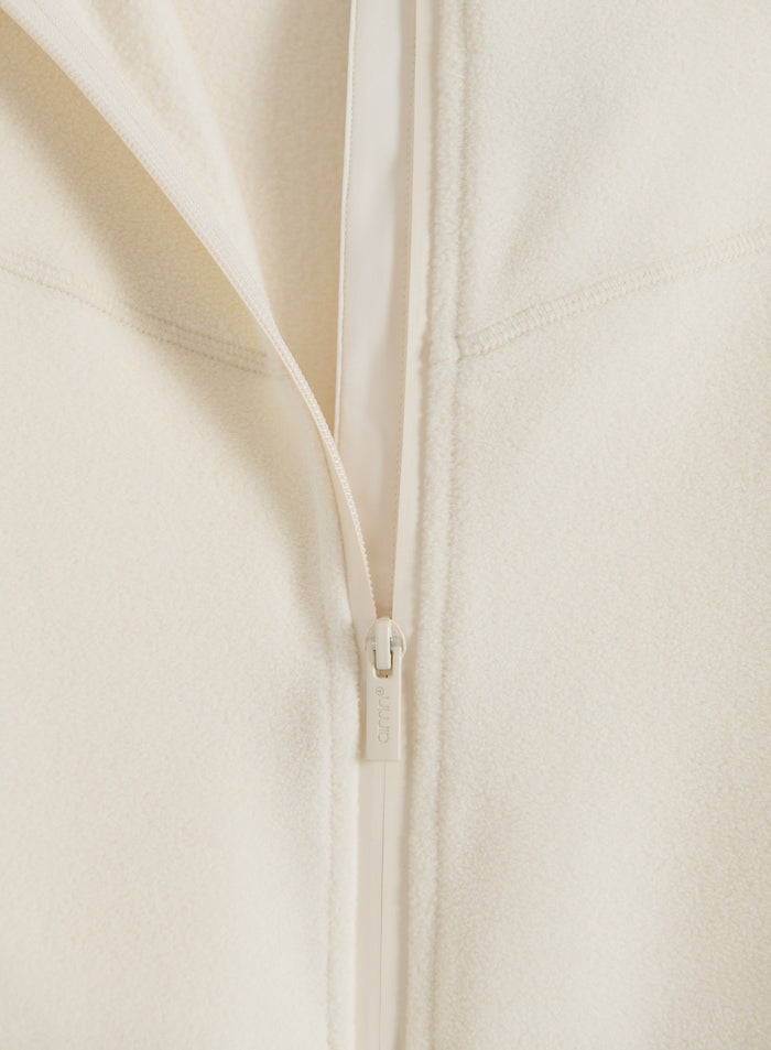 Close-up flatlay of a cream Stretch Fleece Zip Jacket showing the soft fleece fabric and front zipper