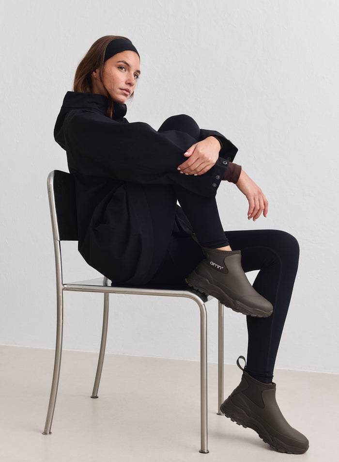 Dark ivy Fusion Rain Boots by aim'n featuring chunky sneaker outsoles, worn by a model on a chair.