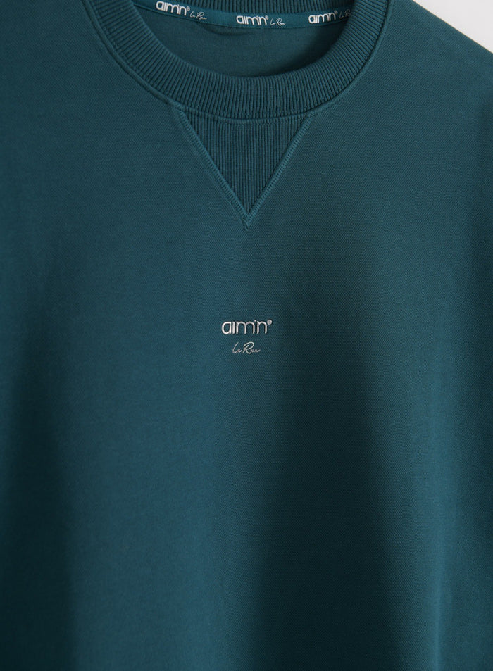Close-up of the front collar and embroidered logo of the aim'n Le Run Running Sweatshirt in lagoon