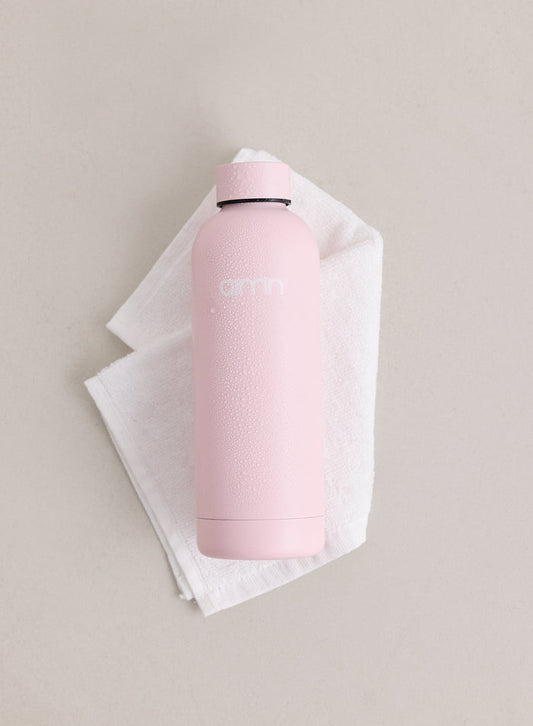 A light pink matte Core Water Bottle featuring the aim'n logo and water droplets, resting on a white towel.