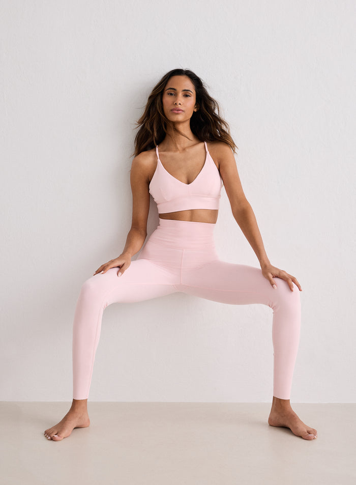 A model wearing Ballerina Sense Petite Tights and a matching sports bra while sitting against a white wall
