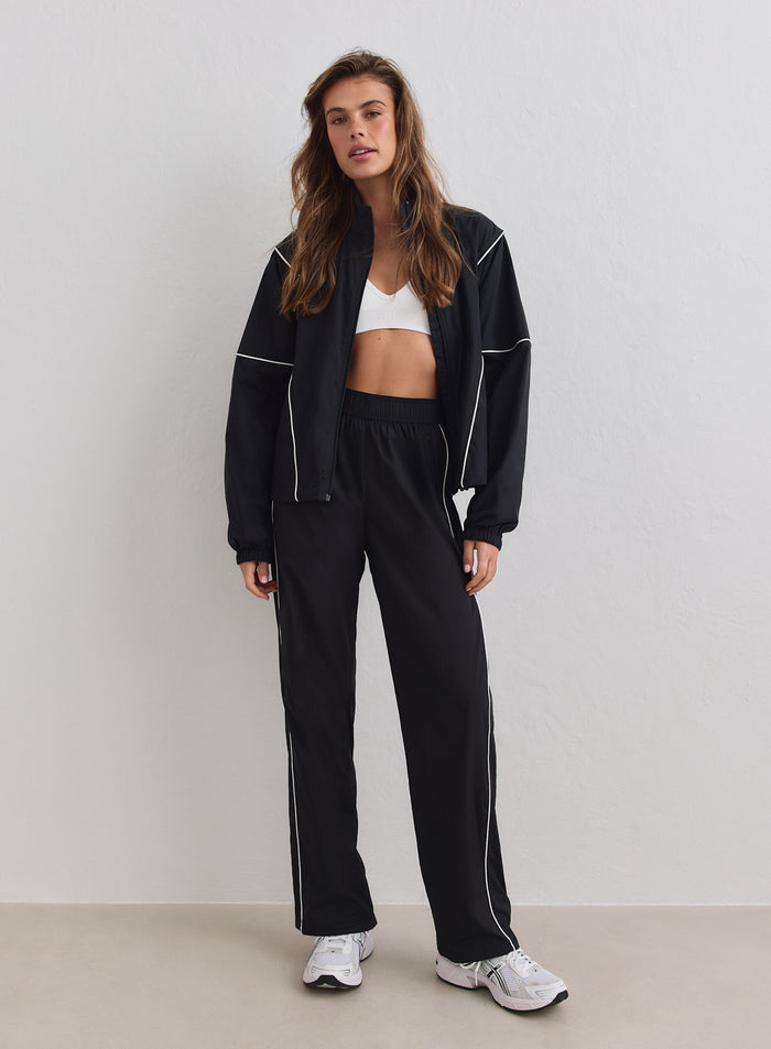 Black Balance Windstopper Tracksuit Jacket with white piping by aim'n, worn open with matching pants and sports bra.