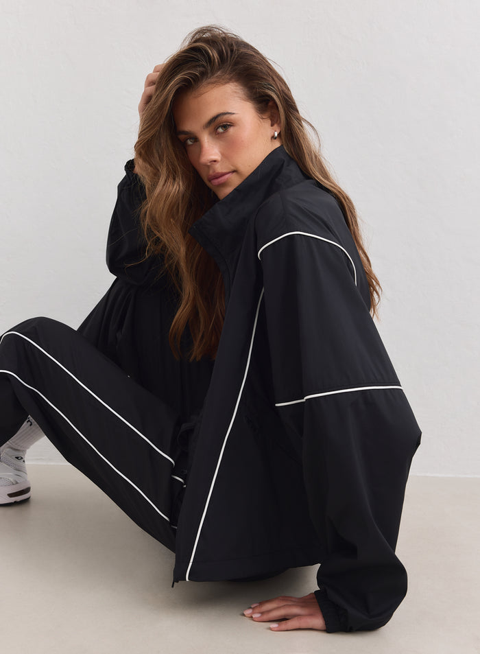 Woman wearing a black aim'n Balance Windstopper Tracksuit Jacket with white piping and a high collar.