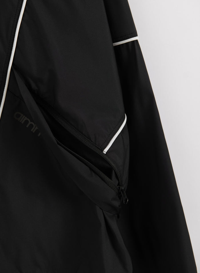 Black Balance Windstopper Tracksuit Jacket detail featuring a zippered pocket, white piping, and aim'n logo.