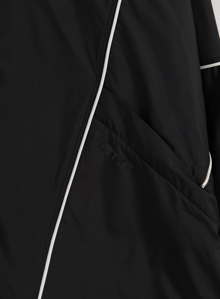 Detail of the black Balance Windstopper Tracksuit Jacket featuring white piping and a tonal aim'n logo.