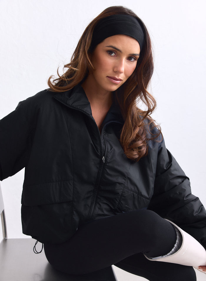 Model sits wearing the black woven Cloud Jacket by aim'n with a headband and leggings. [S-163cm]