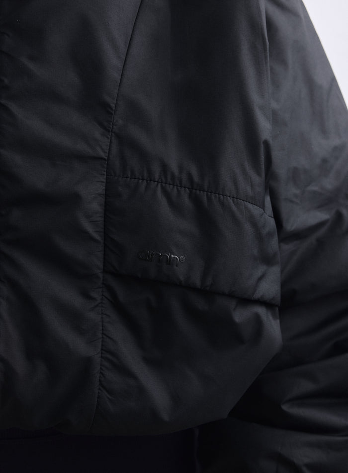 Black Cloud Jacket close-up showing woven fabric, pocket detail, and tone-on-tone aim'n logo. [S-163cm]