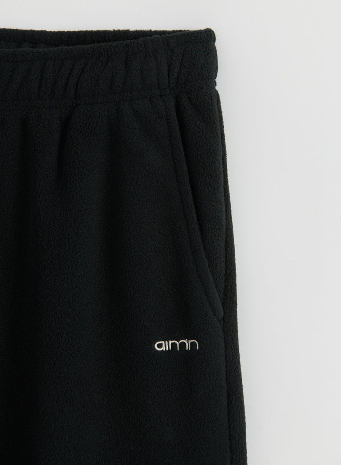 Close-up of black aim'n fleece pants showing the elastic waistband, side pocket, textured fabric, and logo