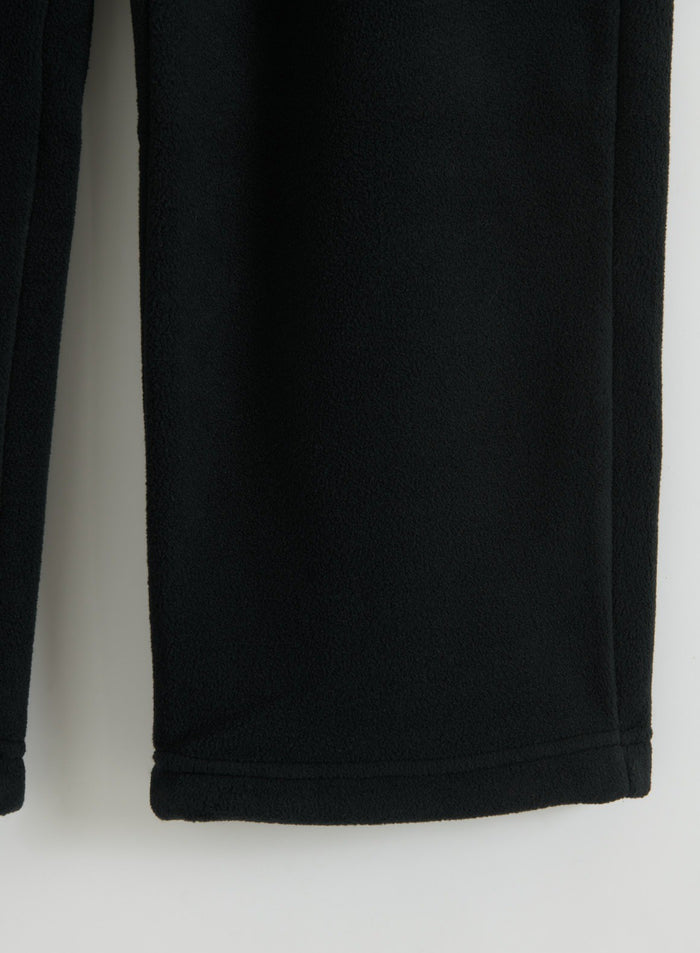 Close-up of black fleece pants showing the soft textured fabric and finished hem