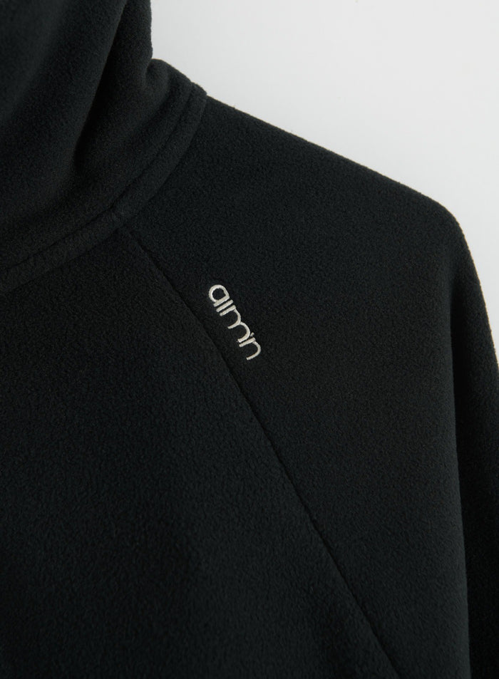 Close-up of a black fleece zip jacket with textured fabric and aim'n logo