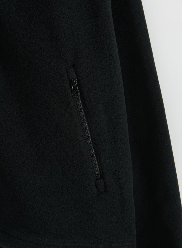 Close-up of a black fleece jacket with a zippered pocket and soft textured fabric