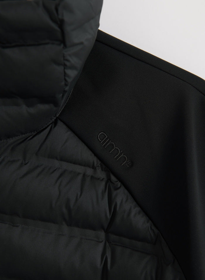 Close-up of a black hybrid jacket showing quilted insulated panels, stretch fabric, and the aim'n logo