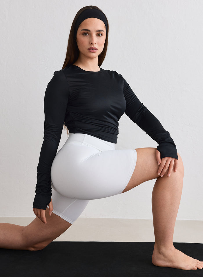 A model wearing a black Luminous Draped Long Sleeve by aim'n and white shorts while performing a lunge [L-174cm]