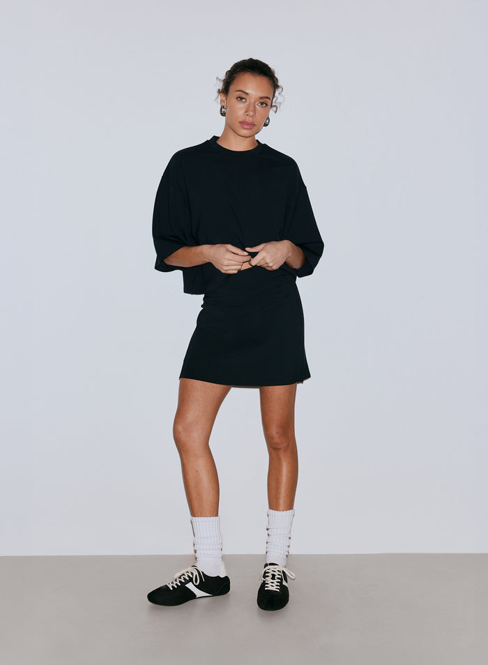 A female model wearing a black oversized top and a black mini skort, white socks, and sneakers. [36-170CM]