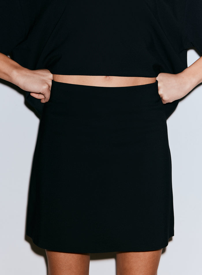 Close-up of a person wearing a black Luxe Mini Skort, pulling the waistband up [36-170CM]
