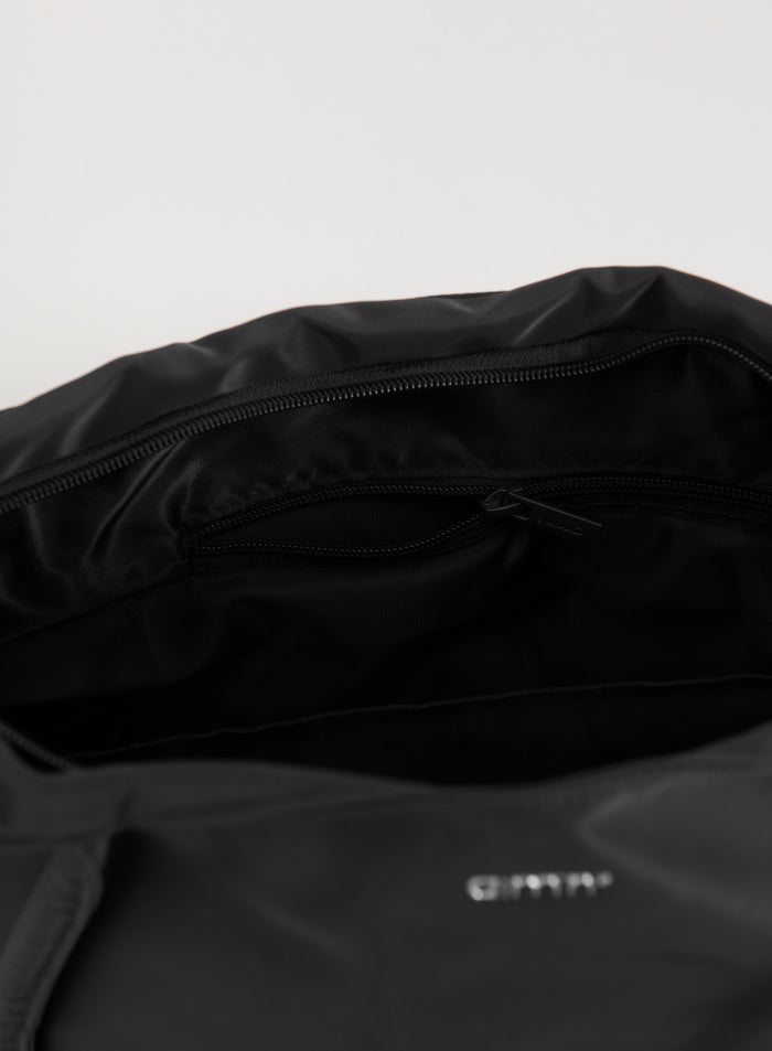 Interior view of the black nylon tote bag featuring a zippered pocket and silver aim'n logo.