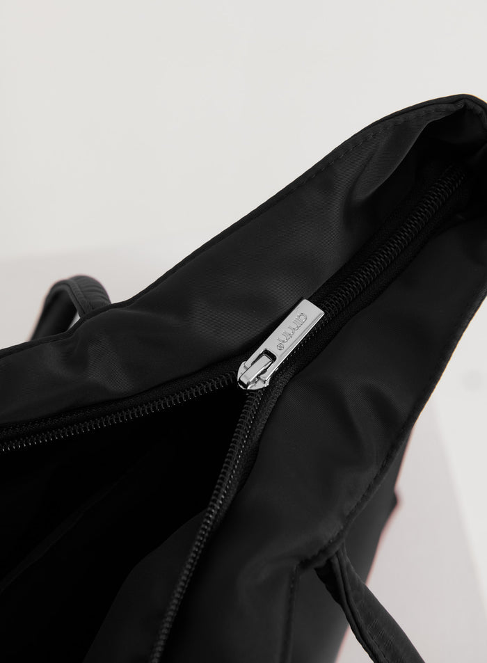 Black nylon tote bag showing a close-up of the silver zipper with an engraved aim'n logo.