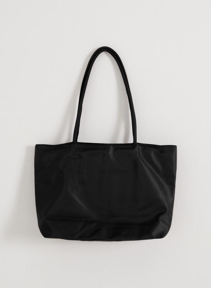 Sleek black nylon tote bag from aim'n with long straps hanging against a plain white wall