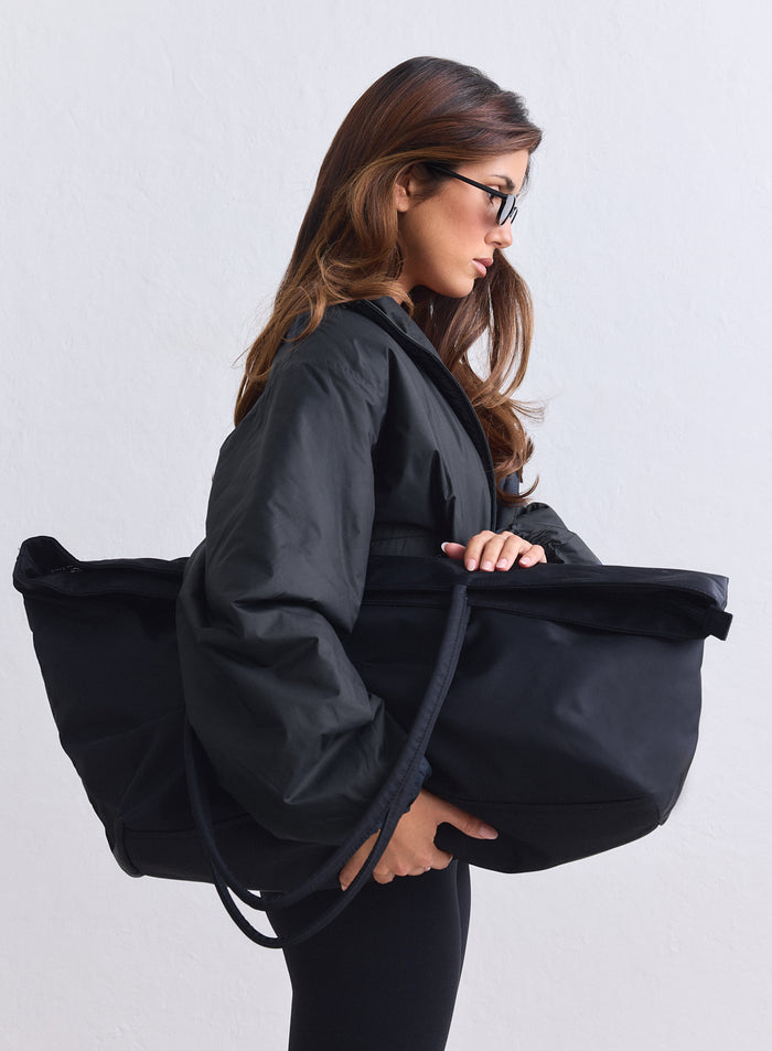 Large black nylon weekend bag by aim'n carried by a woman in a sleek profile view.