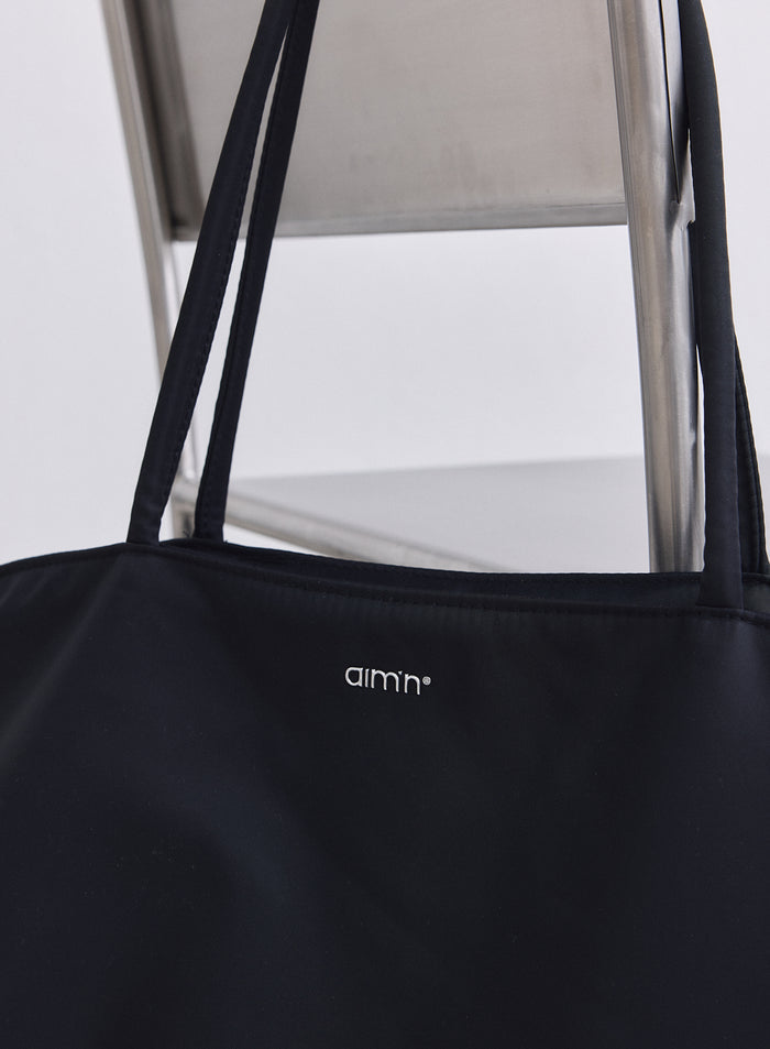 Black nylon weekend bag featuring a small white aim'n logo and long shoulder straps.