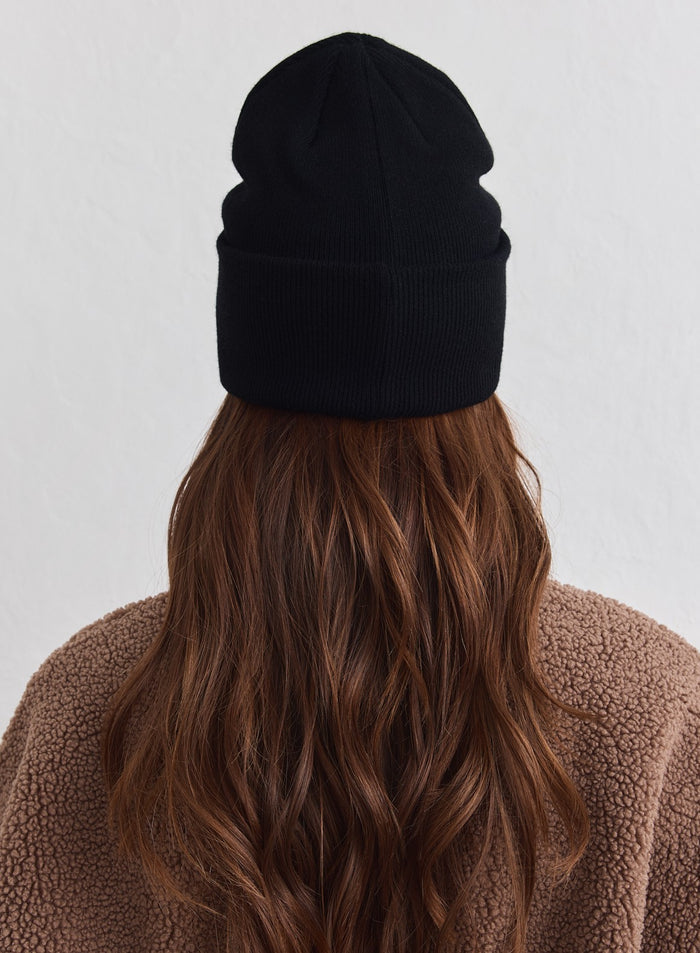 Black knit Outdoor Logo Beanie from aim'n shown from the back on a model wearing a brown fleece jacket.