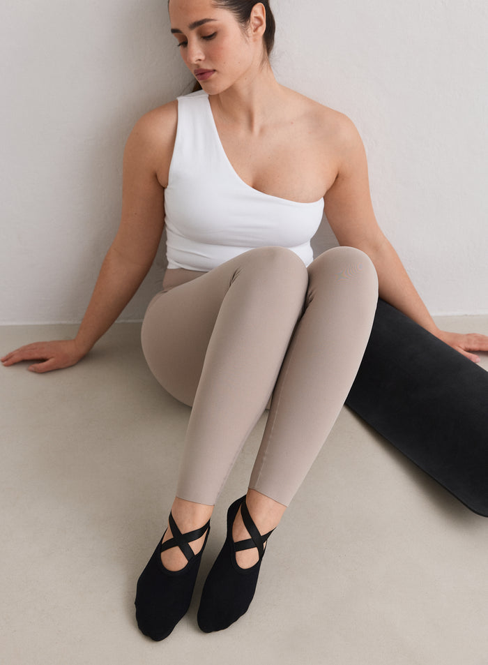 A model wearing Black Pilates Socks from aim'n sitting on the floor
