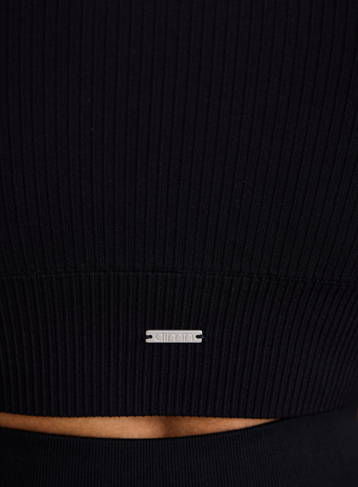 Close-up of the metal aim'n logo badge on the Black Ribbed Seamless Crop Top [XS-170cm]