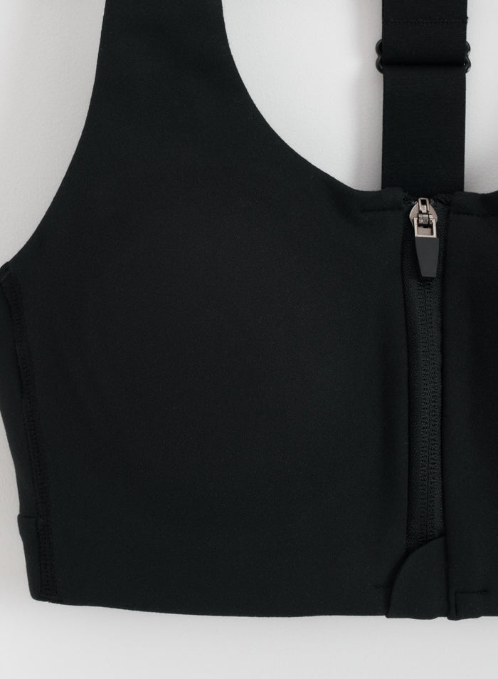 Detail view of the front zipper and adjustable strap on the black Sense High Support Bra by aim'n.