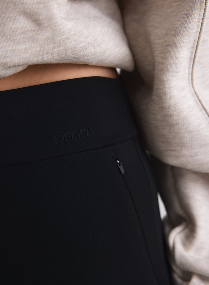 Close-up of black Sense Tall Pants featuring the aim'n logo and a discreet zipped pocket. [M-170cm]