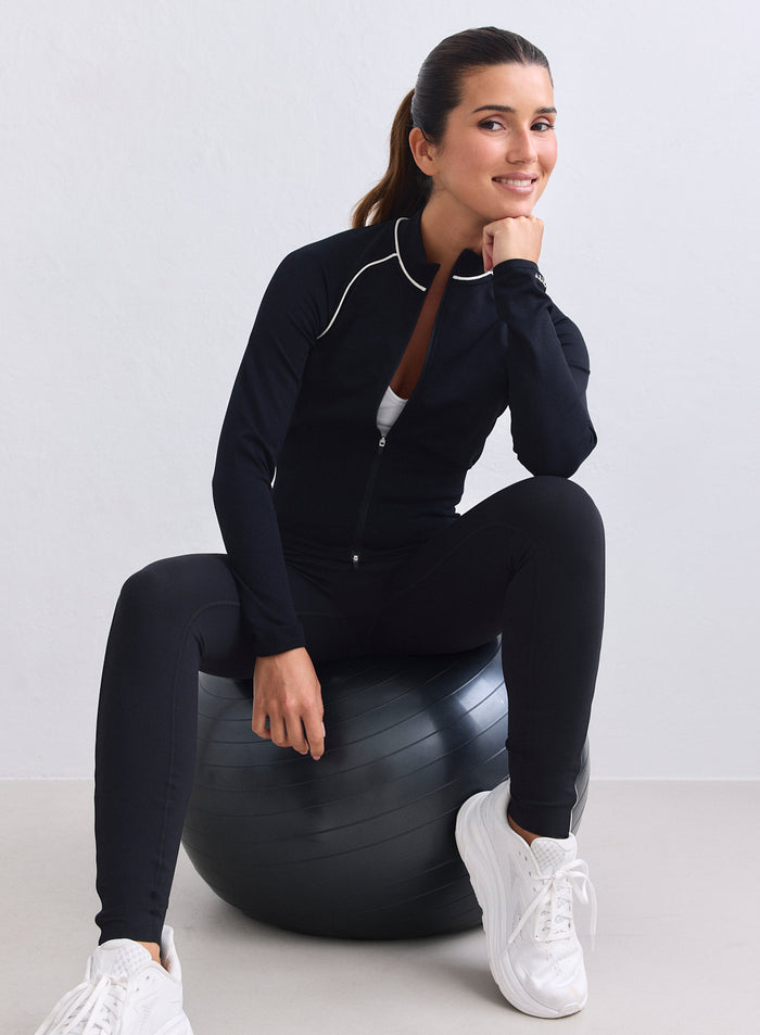 Black aim'n Shape Seamless Contrast Zip Jacket with white piping worn by a model on an exercise ball. [XS-165cm]