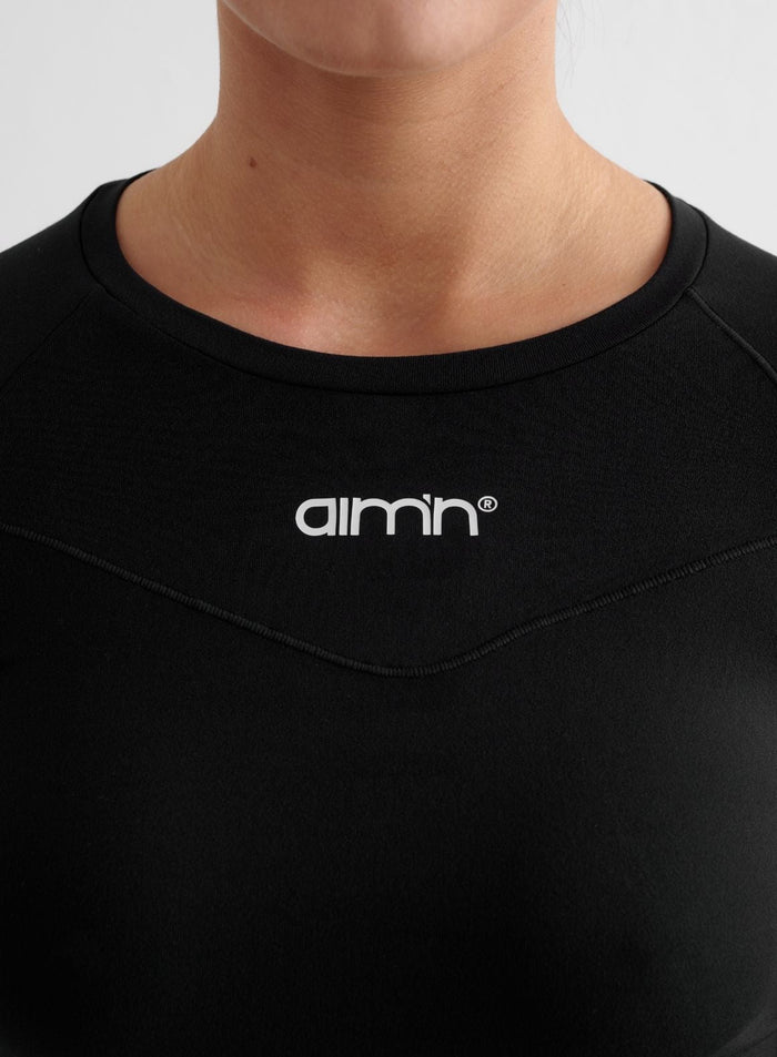Close-up of a black Soft Basic Long Sleeve with a white aim'n logo and pintuck detailing.