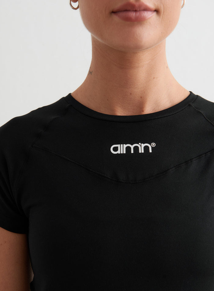 Black Soft Basic Short Sleeve featuring a white aim'n logo and flattering pintuck shaping detail.