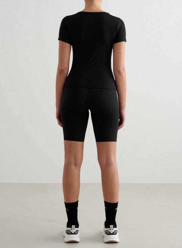 Tight-fitting black short-sleeved training top from aim'n, styled with matching biker shorts, back view.