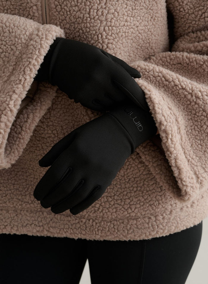Black warming gloves featuring a tonal aim'n logo, paired with a cozy beige fleece jacket.