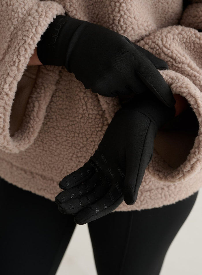 Black Warming Gloves with grip print and a tonal logo, styled with a beige fleece jacket for outdoor comfort by aim'n.