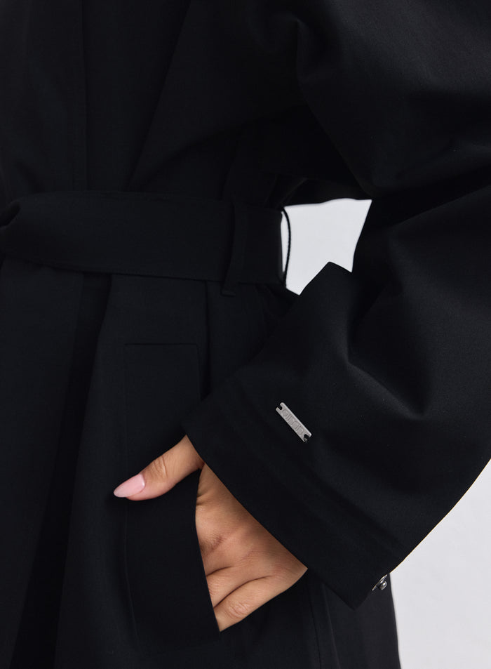 Close-up of a black waterproof coat by aim'n with a belted waist and sleeve logo. [S-165cm]