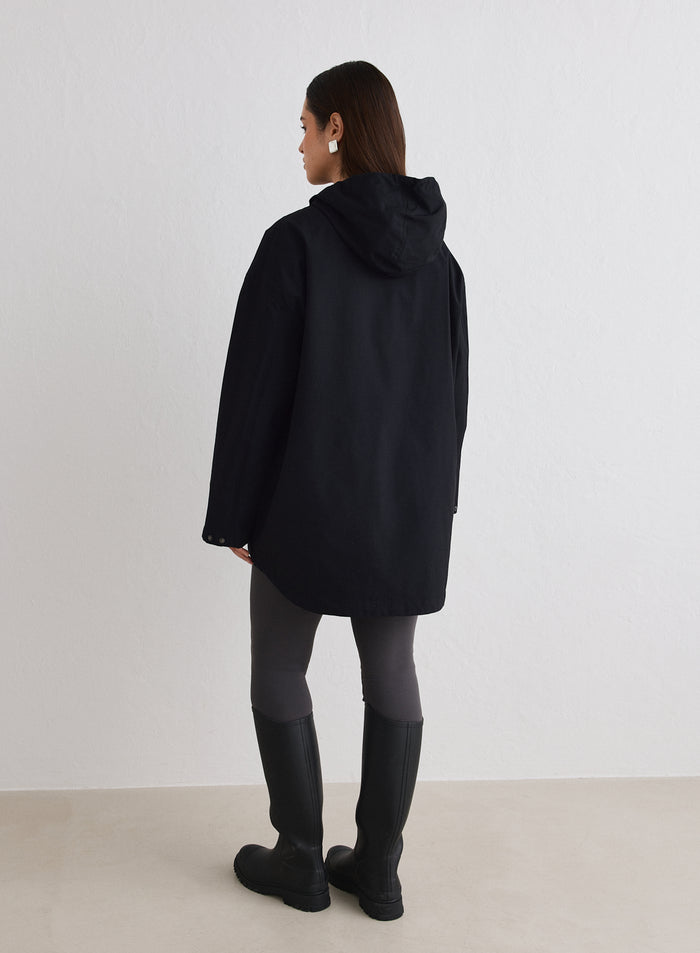Back view of a woman wearing a Black Waterproof Oversized Anorak, dark leggings, and black boots [M-174cm]