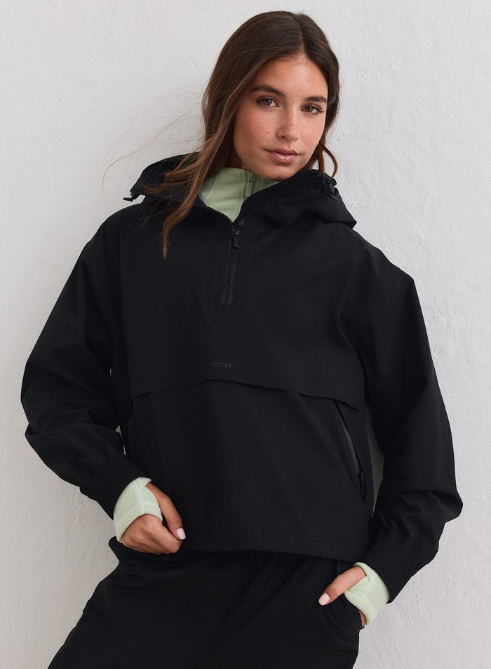 Black Waterproof Stretch Anorak by aim'n with a hood and half-zip, layered over a light green top. [xs-178cm]