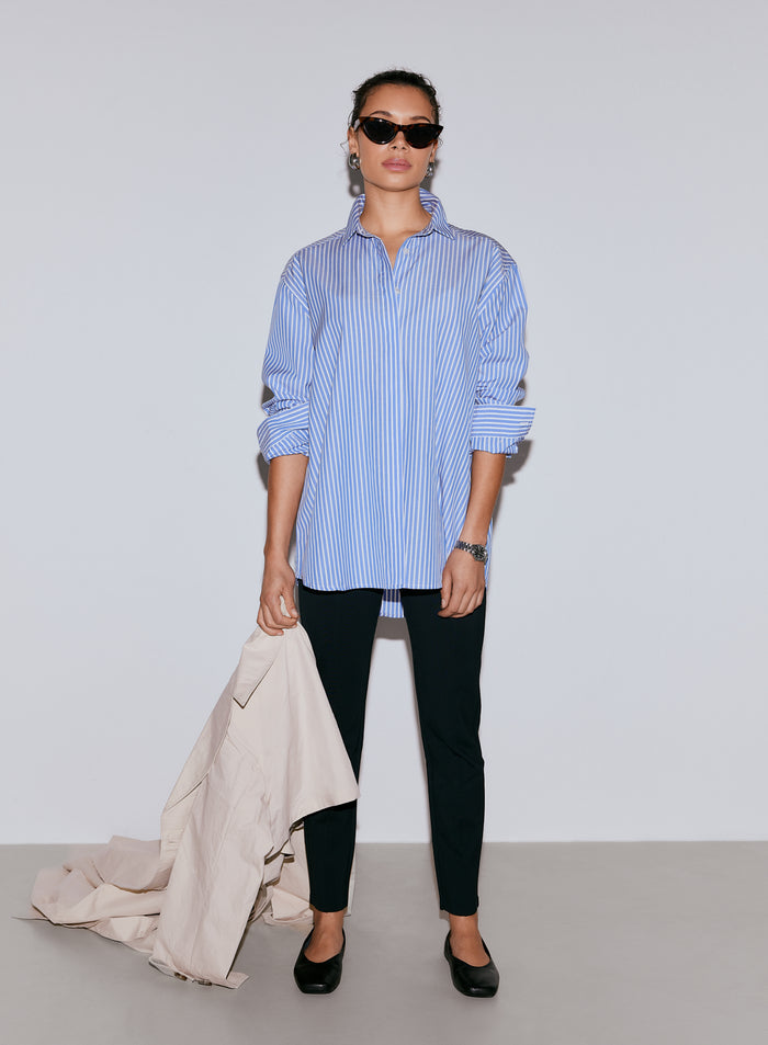 A model wearing an oversized blue striped poplin shirt, black trousers, and sunglasses, holding a light-colored jacket [M-170cm]