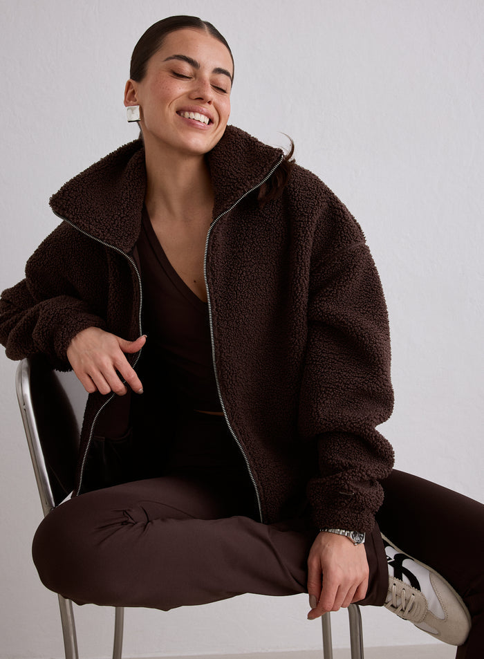 A woman sitting on a chair wearing a Cacao Pile Jacket from aim'n [M-174cm]