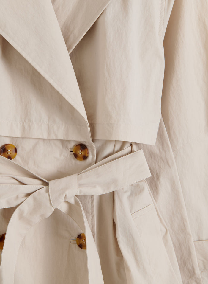 Café au lait aim'n Femme Trenchcoat detail featuring tortoiseshell buttons, a tied waist belt, and storm flaps.