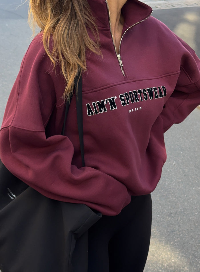 Cherry red relaxed-fit half-zip sweatshirt featuring a stand collar and varsity-style aim'n chest embroidery.