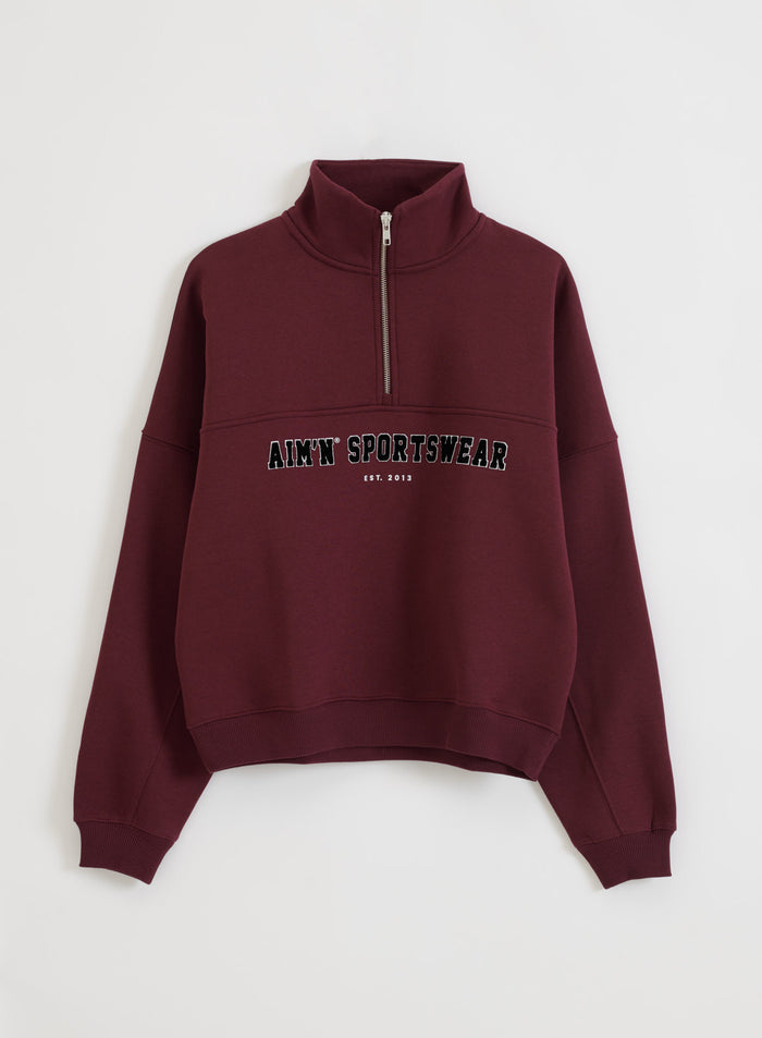Relaxed cherry red Varsity Sweat Half Zip featuring a varsity-style aim'n print and stand collar flatlay.