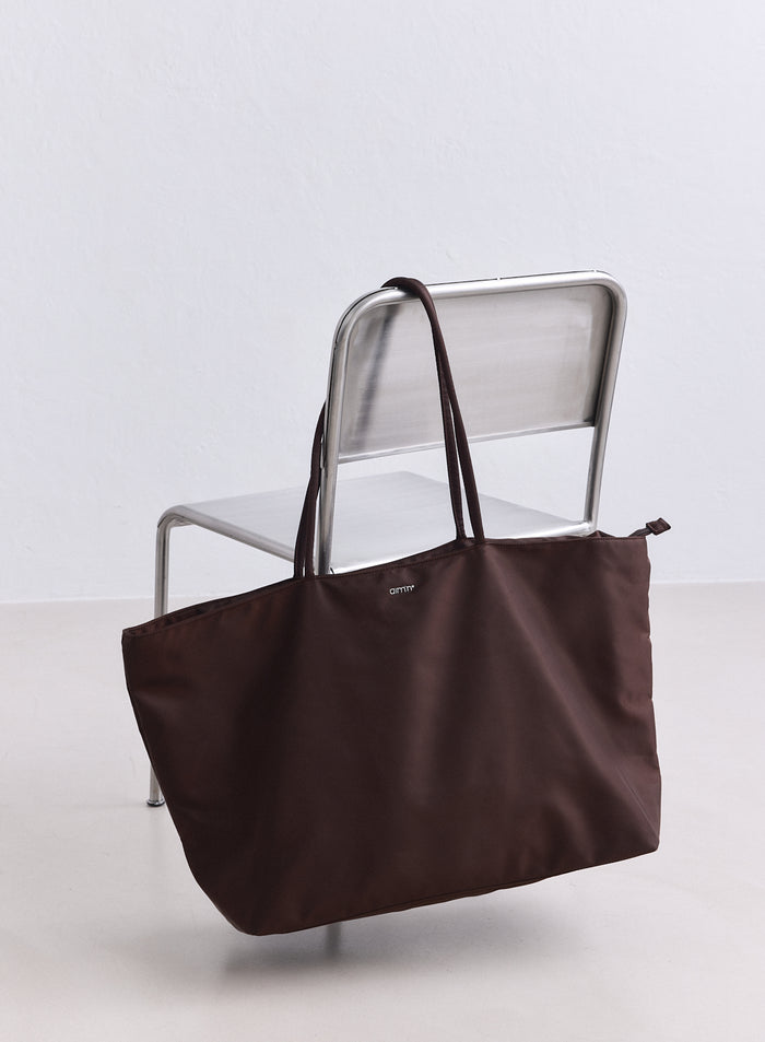 Chocolate nylon weekend bag by aim'n hanging on a sleek silver chair.