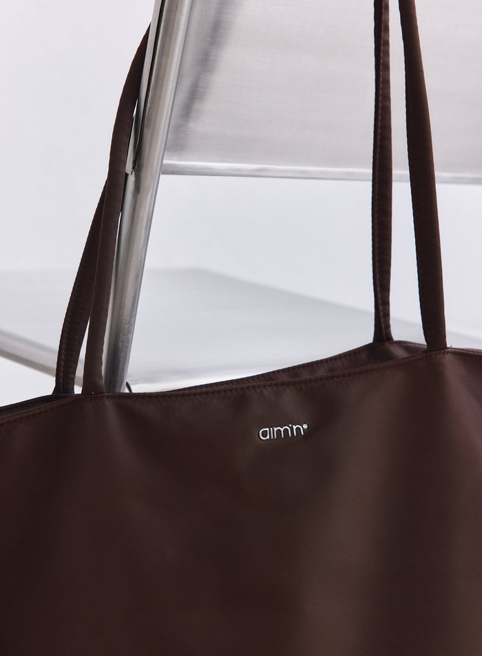 Chocolate brown nylon weekend bag featuring long straps and a silver aim'n logo on the front.
