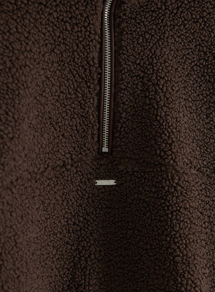 Close-up of a chocolate-brown pile fleece half-zip with a silver zipper and aim'n logo