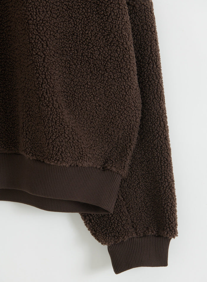 Close-up of a chocolate brown pile fleece jacket with textured fabric and ribbed cuffs