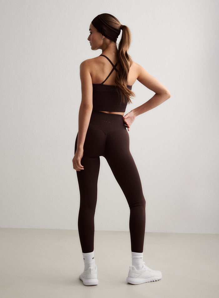 Back view of a woman wearing chocolate brown Shape Seamless Tall Tights and a matching sports bra [S-174cm]