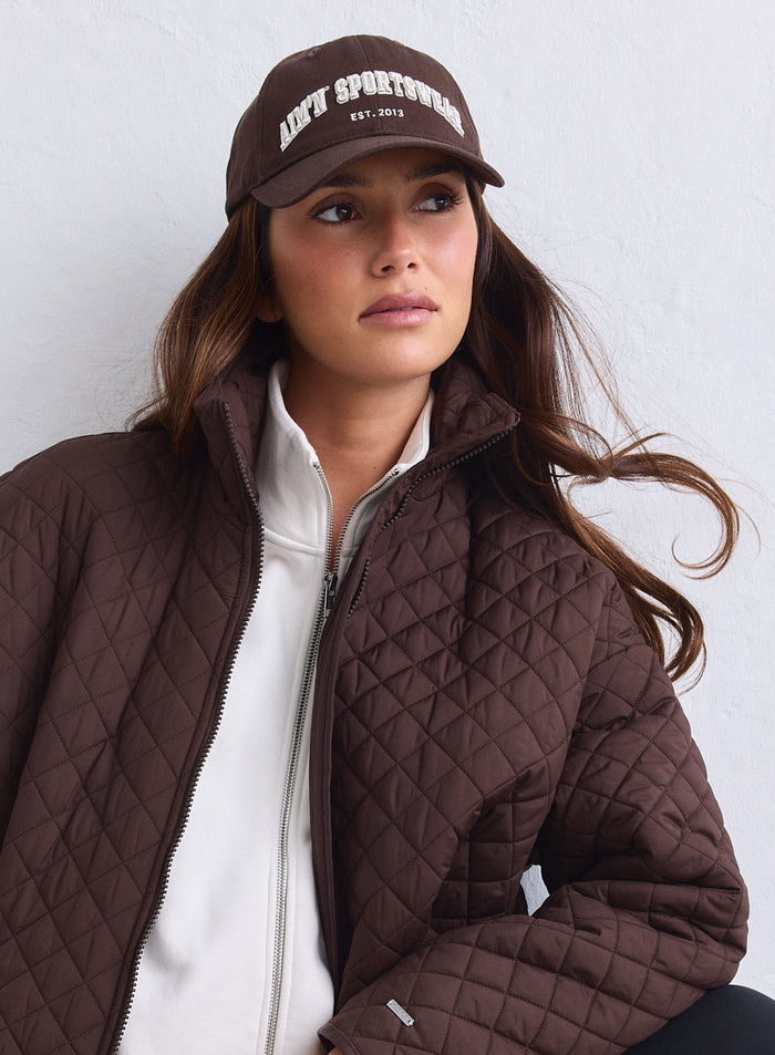 Chocolate brown cotton aim'n Varsity Cap with white embroidered logo worn by a woman.