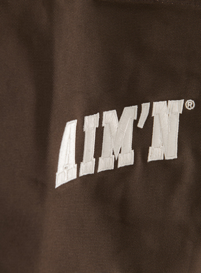 White embroidered varsity logo on a chocolate brown cotton canvas aim'n tote bag.